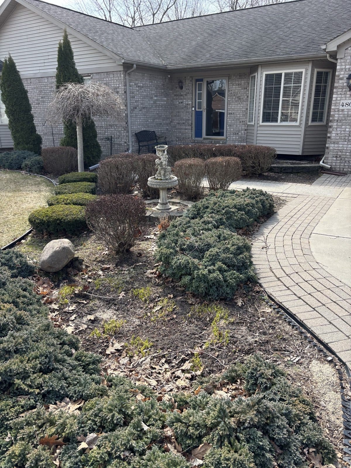 Brick ranch home with a curved paver walkway, stone fountain, and shaped evergreen beds installed by J. Molina Landscaping