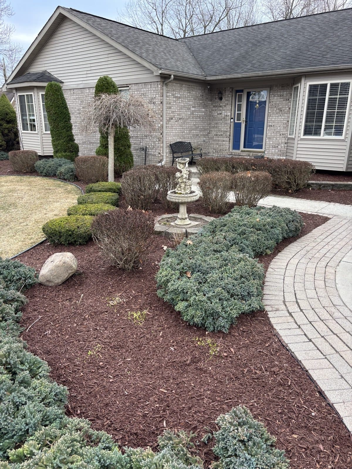 Curved interlocking-paver walkway leading to a home's entrance, bordered by fresh mulch beds and a stone fountain, built by J. Molina Landscaping