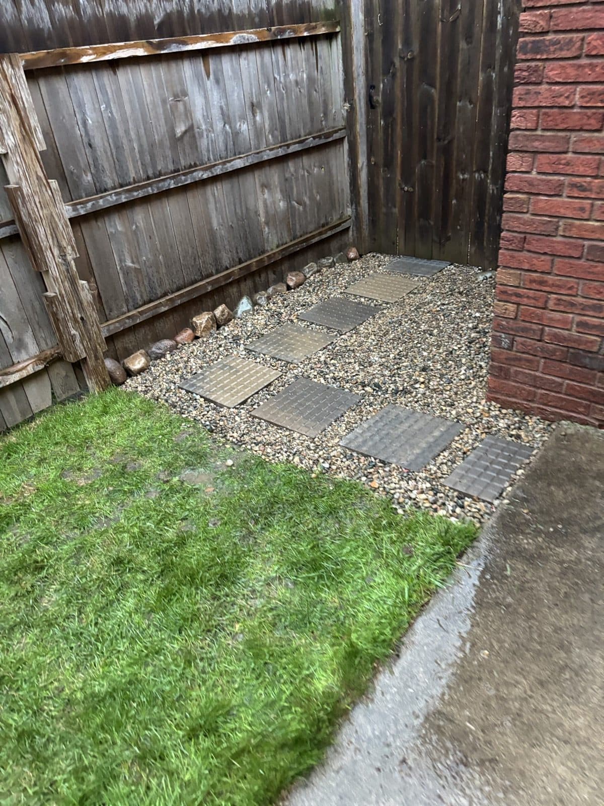 Backyard corner with a wood privacy fence, tidy lawn, and a clean gravel and stone border strip